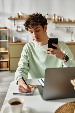 Odaklanmış genç bir adam masasına notlar yazar. Şık bir yaşam alanındaki iş ve teknolojiyi dengeler..