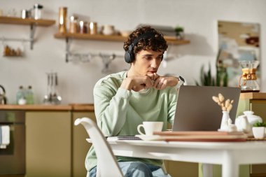 Genç bir adam dizüstü bilgisayarının başında çalışıyor, şık çalışma alanındaki görevlere dalmış..