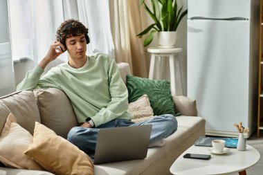 Yakışıklı bir genç adam evinde huzurlu bir öğleden sonranın tadını çıkarırken rahat bir şekilde kanepede oturur ve dizüstü bilgisayarıyla çalışır..