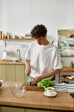 Kıvırcık saçlı genç bir adam modern mutfağında canlı bir salata yaratıyor ve sağlıklı bir hayatı kucaklıyor..