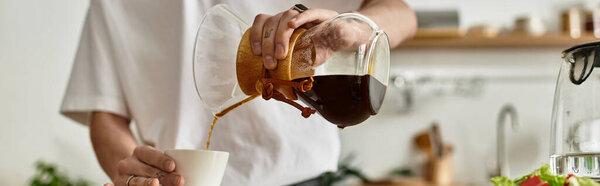 A young man carefully pours fresh coffee into a small cup in his warm kitchen.