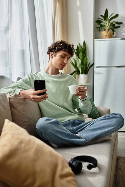 Молодой человек расслабляется в своей стильной квартире, работая по телефону, потягивая из миски.