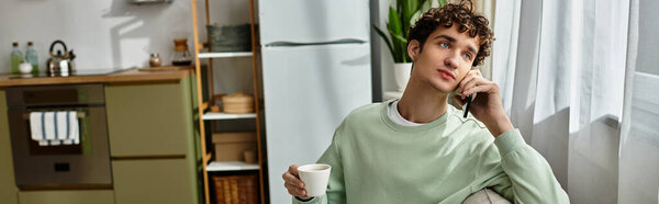 Красивый молодой человек говорит по телефону, потягивая кофе в современном, ярком жилом помещении.