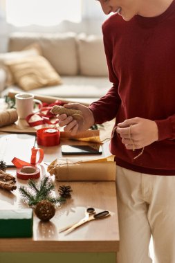 Genç bir adam Noel hediyelerini dekorasyon ve malzemelerle dolu bir şenlik masasında paketlemekten hoşlanır..