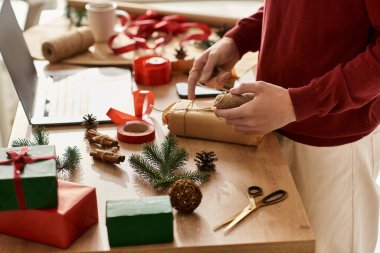 The young man engages in gift wrapping, surrounded by holiday decorations and cheerful elements. clipart