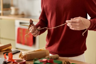 A young man wraps Christmas gifts with care in a warm and inviting kitchen atmosphere. clipart