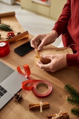 Genç bir adam, dekoratif eşyalar ve malzemelerle çevrili Noel hediyelerini ustalıkla paketliyor..