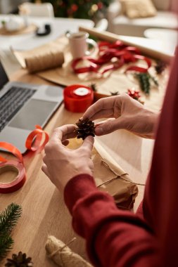 Genç bir adam güzel paketlenmiş bir Noel hediyesine dikkatlice çam kozalağı ekler..