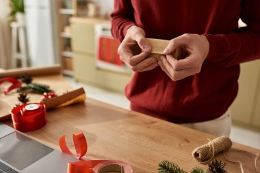 Genç adam, neşeli süslemeler ve sıcaklıkla çevrili Noel hediyelerini paketlemekten hoşlanıyor..