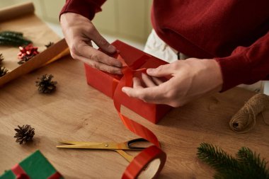 Genç bir adam canlı kırmızı bir Noel hediyesini şenlikli süslemelerle ustalıkla paketliyor..