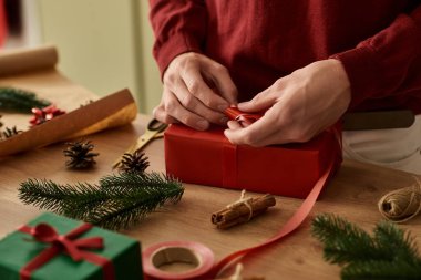 Genç adam, etrafı dekorasyon ve malzemelerle çevrili kırmızı bir hediyeyi paketlemekten hoşlanıyor..