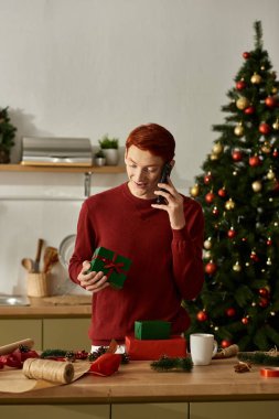 Genç adam Noel hediyelerini sıcacık bir ortamda paketlerken birine telefon ederken gülümsüyor..