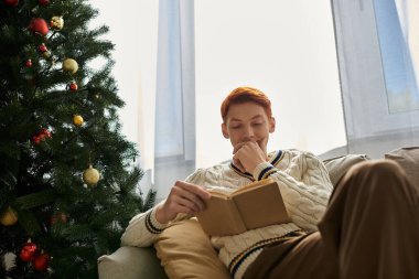 Genç adam huzur içinde oturuyor, Noel ağacı tarafından okunuyor..