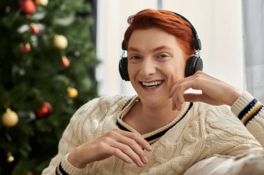 Kızıl saçlı genç bir adam Noel sezonunda müzik dinlerken gülümsüyor..