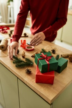 Genç adam tatil süslemeleriyle çevriliyken renkli Noel hediyelerini dikkatlice paketliyor..