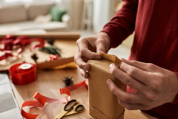 The young man is focused on wrapping a Christmas gift, showcasing his holiday spirit and creativity.