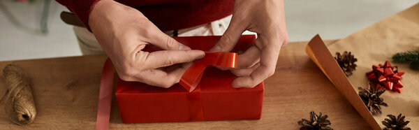 Молодой человек сосредоточен на обертывании рождественского подарка яркой лентой и украшениями..
