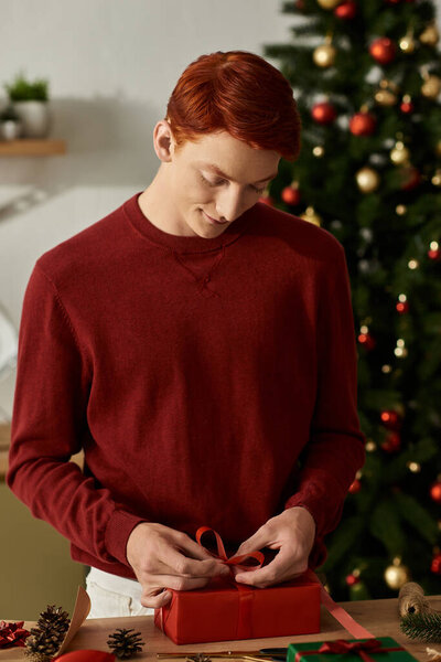 A teenager joyfully adds a ribbon to a red wrapped present surrounded by holiday cheer.