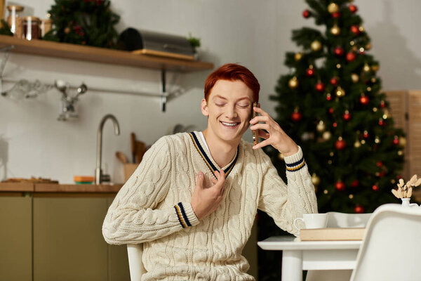 A smiling young man talks on the phone while celebrating Christmas in a cozy setting.