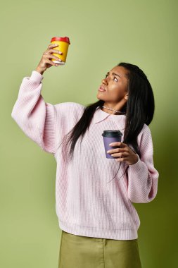 Modaya uygun genç bir kadın merakla bakarken iki sıcak içki tutuyor..