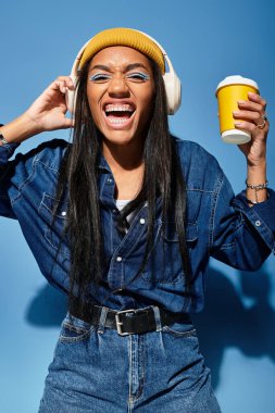 Kulaklıklı şık bir genç kadın elinde kahve fincanı tutarken gülümsüyor..