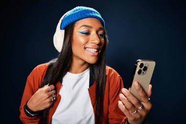 Şık bir sonbahar kıyafeti giyen genç bir kadın müzik dinler ve kapalı alanda gülümser..