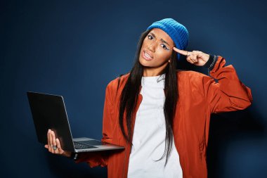 A young woman in a cozy outfit playfully engages with her laptop, showcasing her creativity. clipart