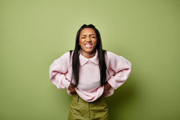 Молодая женщина в уютном осеннем одеянии светится счастьем в ярко-зеленом пространстве.