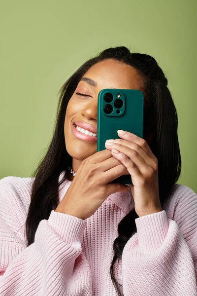 Wearing a stylish sweater, a young woman captures a joyful moment with her phone, smiling brightly.