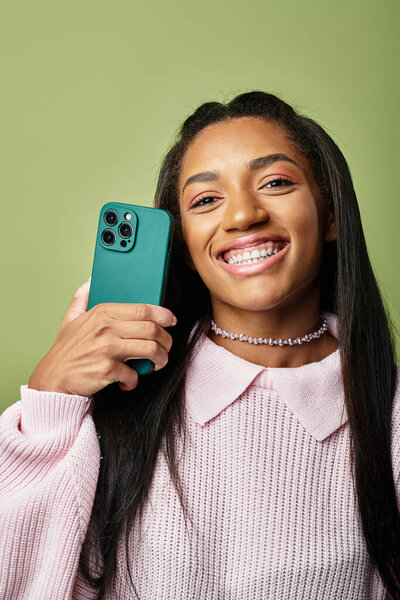 Ярко одетая в теплые слои, молодая женщина радуется, держа в руках смартфон..