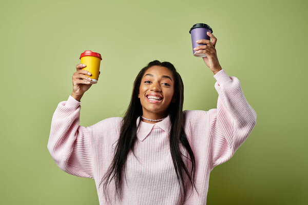 A young woman in autumn attire joyfully holds two colorful cups, embracing the warmth.