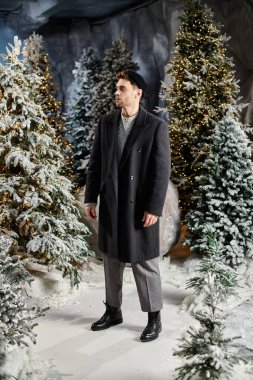 Süslü bir adam, Noel ve yeni yıl kutlamalarının kış ruhunu kucaklayarak, donmuş çam ağaçlarının yanında duruyor..