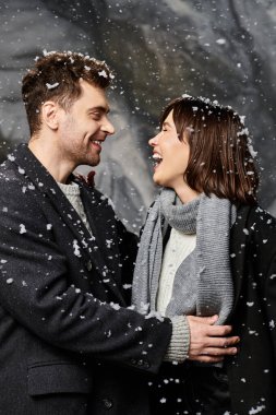 A loving couple embraces joyfully while snow falls around them, celebrating the winter season together. clipart