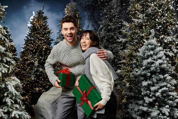 Счастливая пара обнимает дух праздника, окруженный заснеженными деревьями, держа подарки.