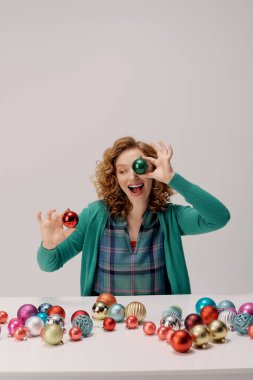 A cheerful young woman organizes vibrant ornaments while preparing for the holiday season. clipart