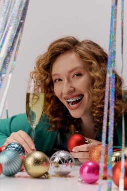 A cheerful young woman prepares gifts while surrounded by festive decorations and sparkling drinks. clipart