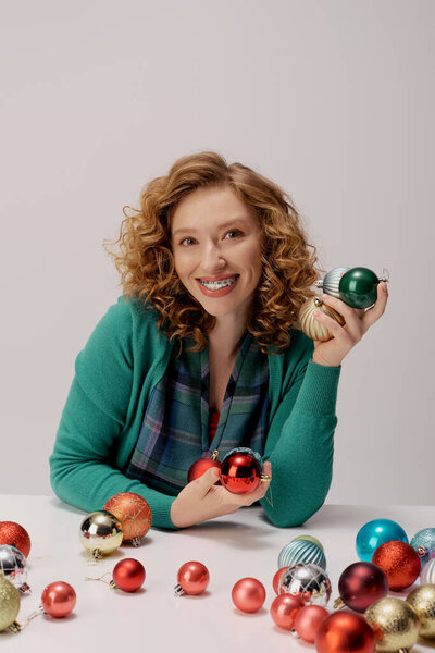 A young woman with curly hair happily holds colorful ornaments while preparing for festivities.