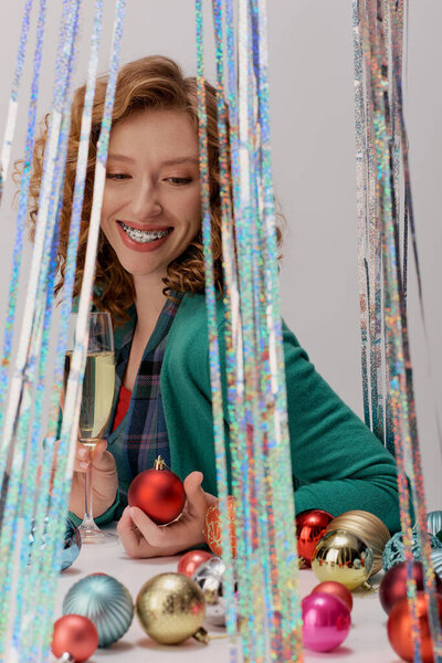 A young woman is cheerfully posing cheerfully surrounded by colorful holiday ornaments and decor.