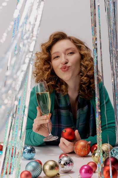 A cheerful young woman holds a glass of sparkling drink surrounded by festive ornaments.