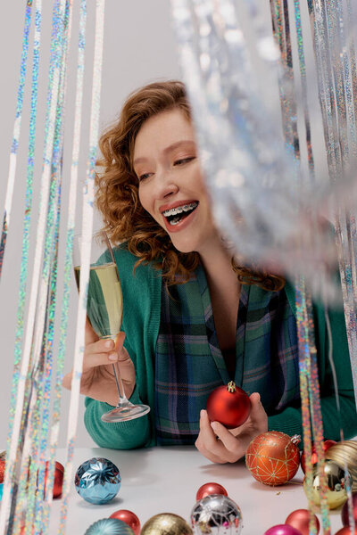 The young woman smiles, posing cheerfully among colorful ornaments and playful decor.