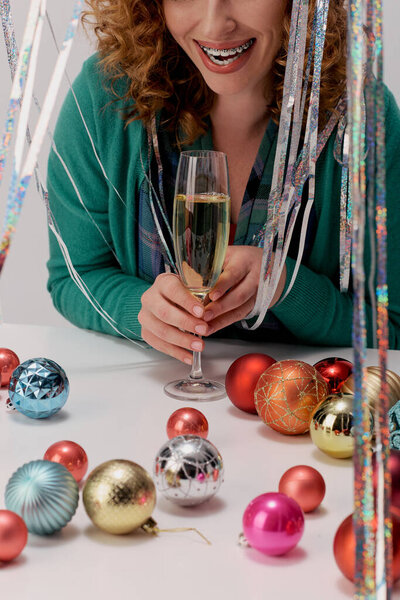 A cheerful young woman enjoys the moment of decorating with colorful ornaments and a drink.