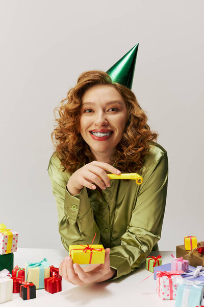 Молодая женщина с вьющимися волосами счастливо позирует в шляпе для вечеринок..