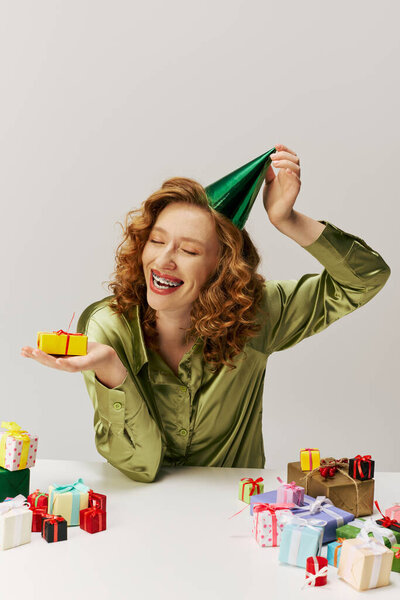 The cheerful woman posing cheerfully in a party hat, surrounded by colorful boxes.