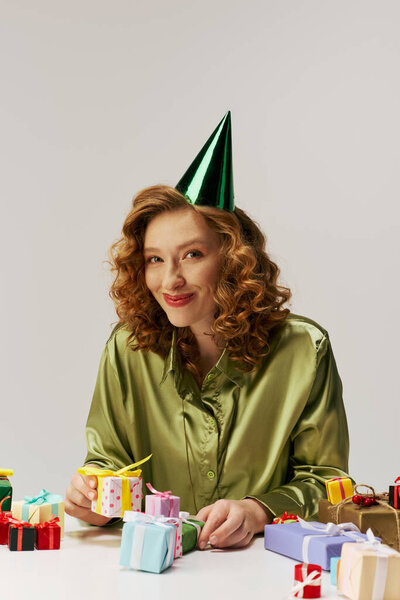 Веселая молодая женщина с вьющимися волосами, творчески позирующая на чистой поверхности.