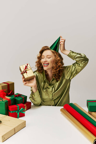 Молодая женщина весело позирует в шляпе и окружена подарками..