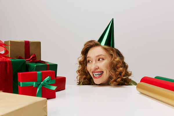 A cheerful girl enjoys posing, surrounded by shiny gift boxes in vibrant colors.