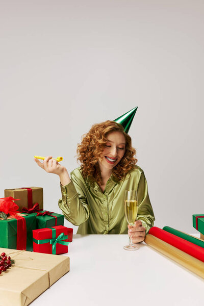 A young woman joyfully posing cheerfully with champagne and a party hat in a festive scene.