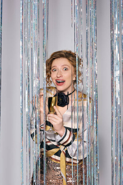 Возбужденная молодая женщина держит завернутый подарок в окружении блестящих украшений, выражая радость.