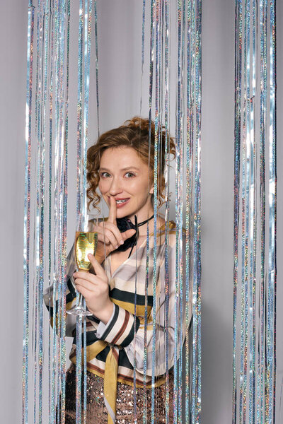 A young woman smiles while posing, surrounded by shimmering decorations.