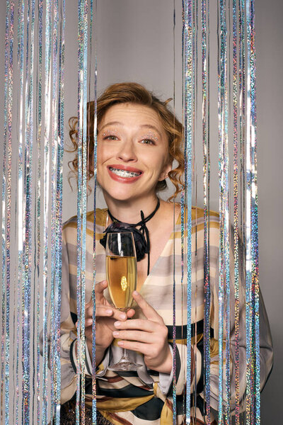A cheerful young woman enjoying a celebration, sparkling drink in hand, with streamers around her.